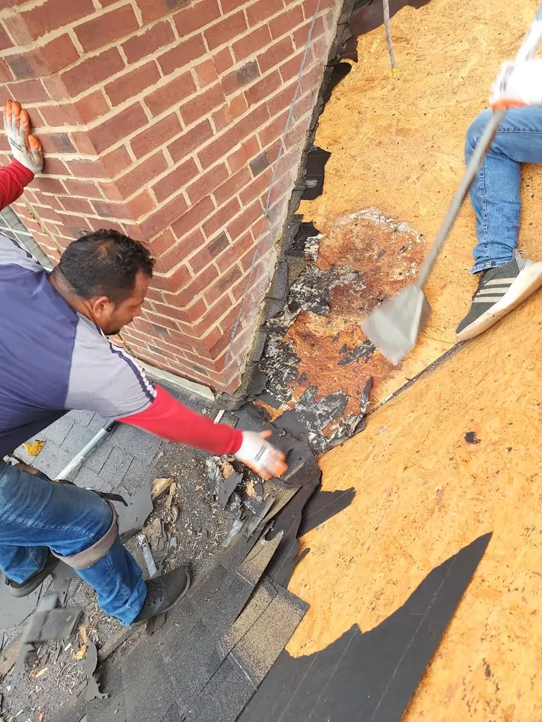 Roof repair tear-off alongside a brick wall